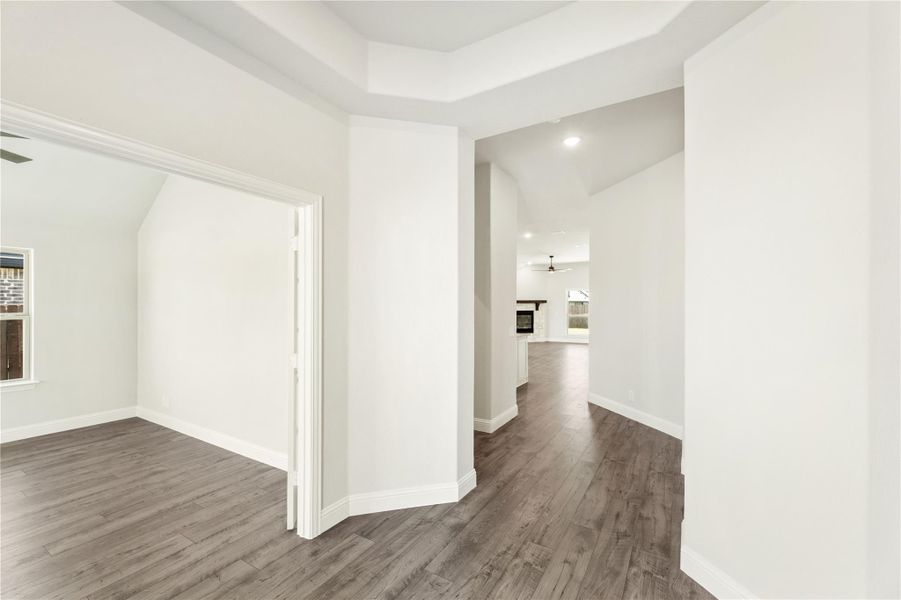 Hallway with dark hardwood floors, white walls, and tray ceiling leading to open living area with fireplace.