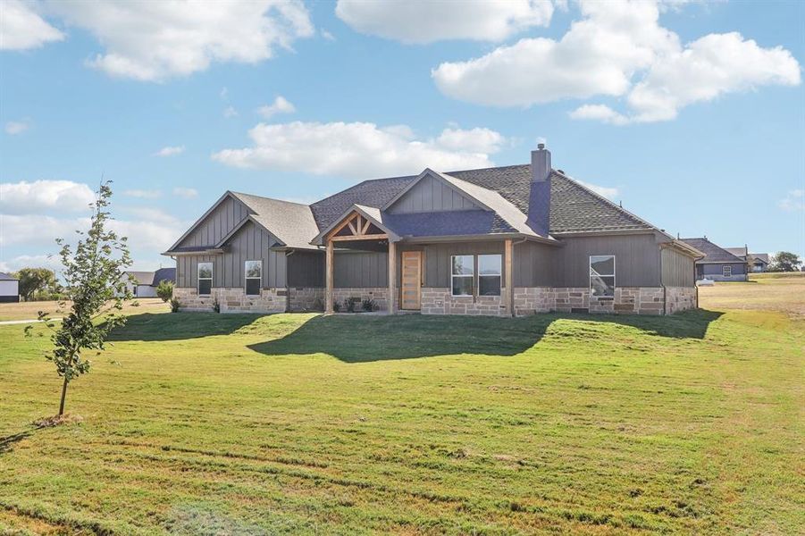 Back of house featuring a chimney, a lawn, a shingled roof, board and batten siding, and stone siding Back of house featuring a chimney, a lawn, a shingled roof, board and batten siding, and stone siding