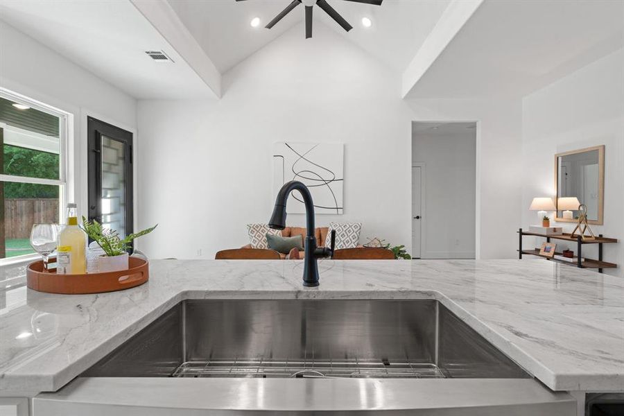 Kitchen featuring lofted ceiling, light stone counters, ceiling fan, and sink