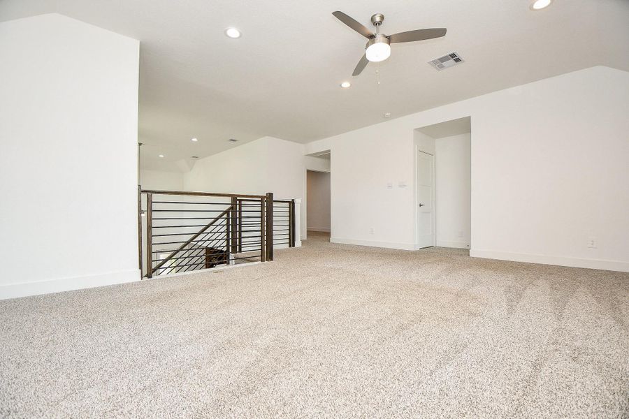 Spacious, carpeted game room equipped with recessed lighting and a ceiling fan. It features a modern iron railing overlooking the stairway, making it ideal for various family activities. Spacious, carpeted game room equipped with recessed lighting and a ceiling fan. It features a modern iron railing overlooking the stairway, making it ideal for various family activities.