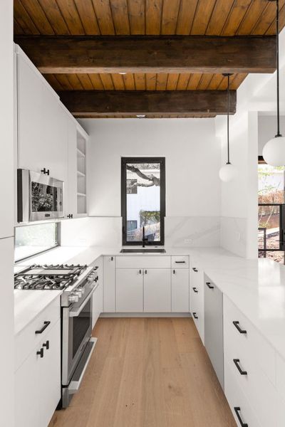 Kitchen with white cabinetry, stainless steel appliances, light wood-style flooring, pendant lighting, and a wooden ceiling with exposed beams