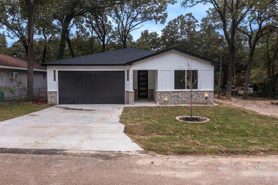 View of front of property featuring brick siding, driveway, a front lawn, board and batten siding, and an attached garage View of front of property featuring brick siding, driveway, a front lawn, board and batten siding, and an attached garage