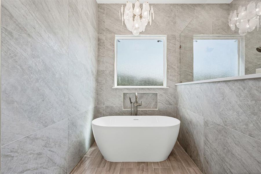 Full bath with a chandelier, tile walls, a freestanding bath, and wood finish floors Full bath with a chandelier, tile walls, a freestanding bath, and wood finish floors