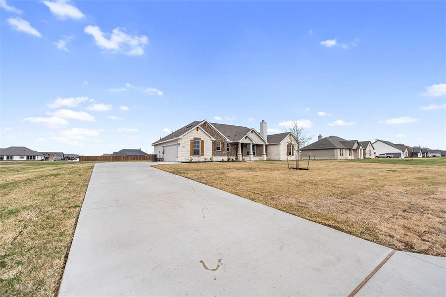 Single story home featuring a residential view, driveway, a chimney, and stone siding Single story home featuring a residential view, driveway, a chimney, and stone siding