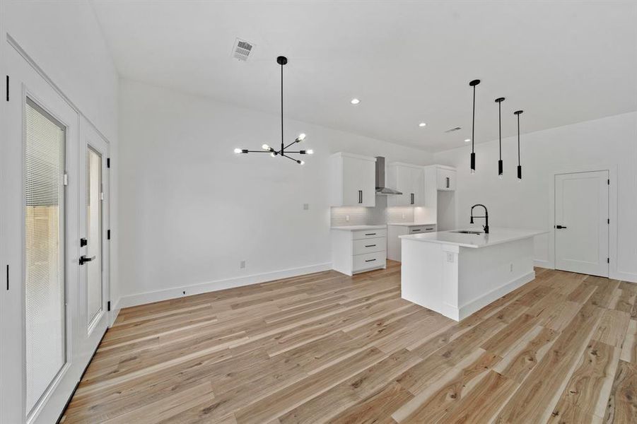 Kitchen with light hardwood / wood-style flooring, white cabinetry, decorative light fixtures, and a center island with sink