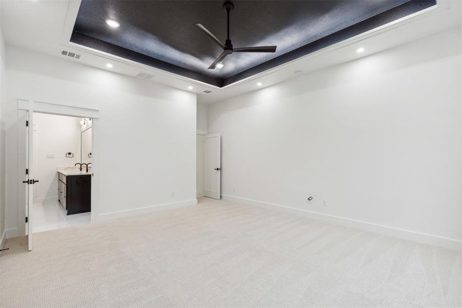 Empty room with sink, light colored carpet, ceiling fan, and a raised ceiling