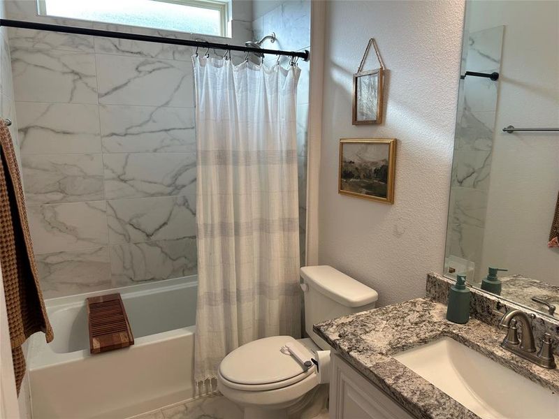 Bathroom with a textured wall, vanity, and shower / tub combo with curtain
