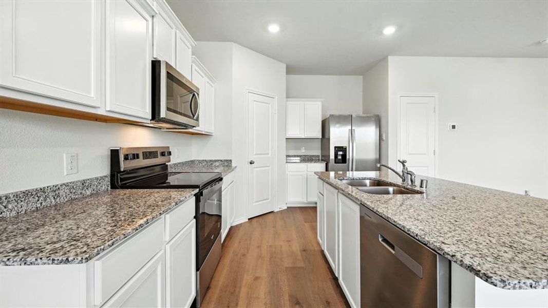 Kitchen featuring white shaker cabinetry, stainless steel appliances, speckled stone countertops, and wood-finish flooring
