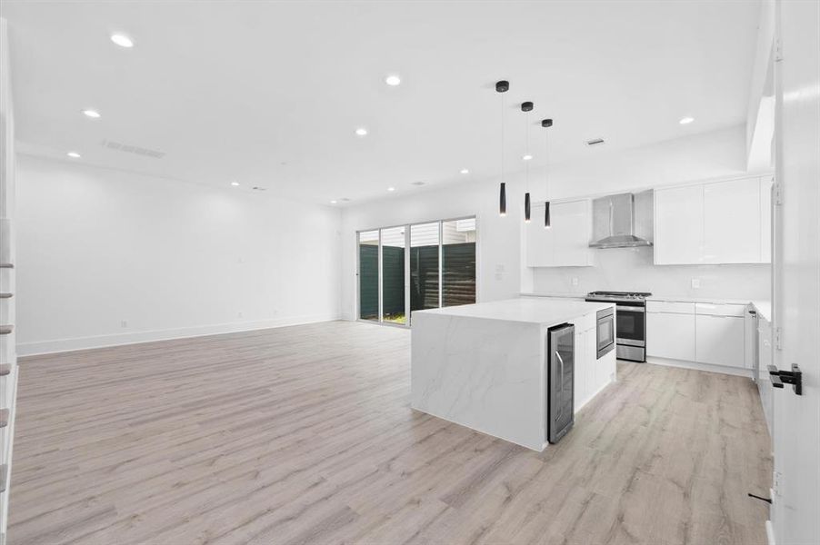 A modern, open-concept kitchen with white cabinetry, stainless steel appliances, and a center island with a Quartz countertop.