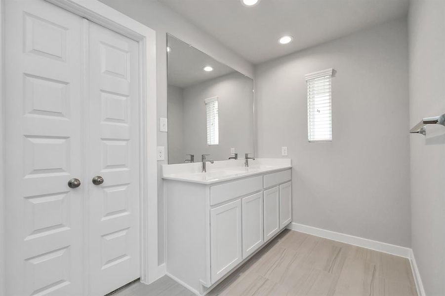 Elevate your daily rituals at the sophisticated vanity, equipped with double sinks, light-hued countertops, contemporary hardware, and recessed lights.