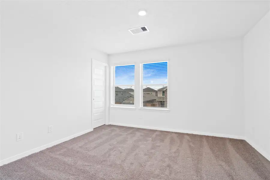 This secondary bedroom offers comfort and style with plush carpeting, neutral paint tones, recessed lighting, large windows with blinds, and a walk-in closet.