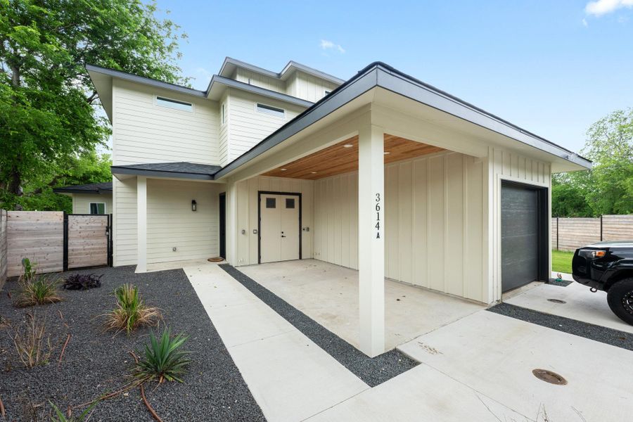 The property features a modern exterior with light-colored siding, a covered entry with a wooden ceiling, and an integrated garage with a black door