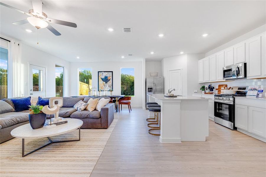 Kitchen featuring white cabinetry, light hardwood / wood-style flooring, a kitchen breakfast bar, stainless steel appliances, and a kitchen island with sink