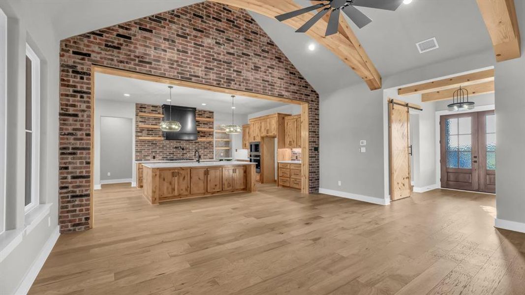 Spacious open-concept living area featuring wood-finish flooring, a vaulted ceiling with exposed wood beams, and a ceiling fan Spacious open-concept living area featuring wood-finish flooring, a vaulted ceiling with exposed wood beams, and a ceiling fan