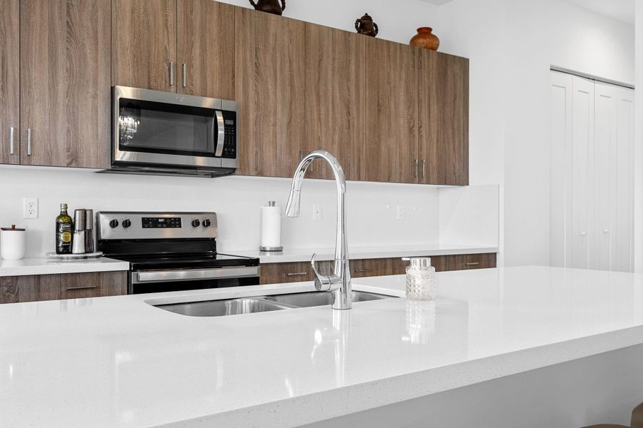 Kitchen with modern cabinets, appliances with stainless steel finishes, light stone countertops, and brown cabinets