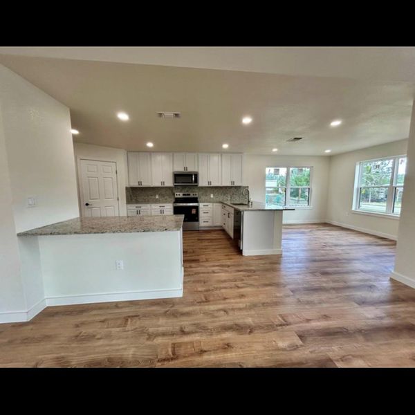 A well-lit kitchen with sleek white cabinetry and granite countertops flows seamlessly into an open living space.