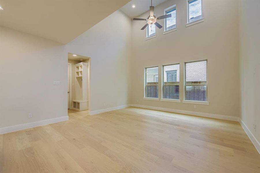 Unfurnished living room featuring light wood-style floors, plenty of natural light, ceiling fan, a towering ceiling, and recessed lighting Unfurnished living room featuring light wood-style floors, plenty of natural light, ceiling fan, a towering ceiling, and recessed lighting