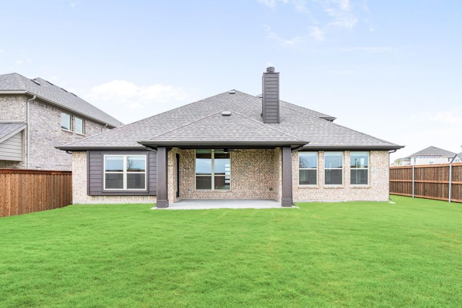 Rear exterior of single-story brick home with covered patio, chimney, and fenced backyard with green lawn