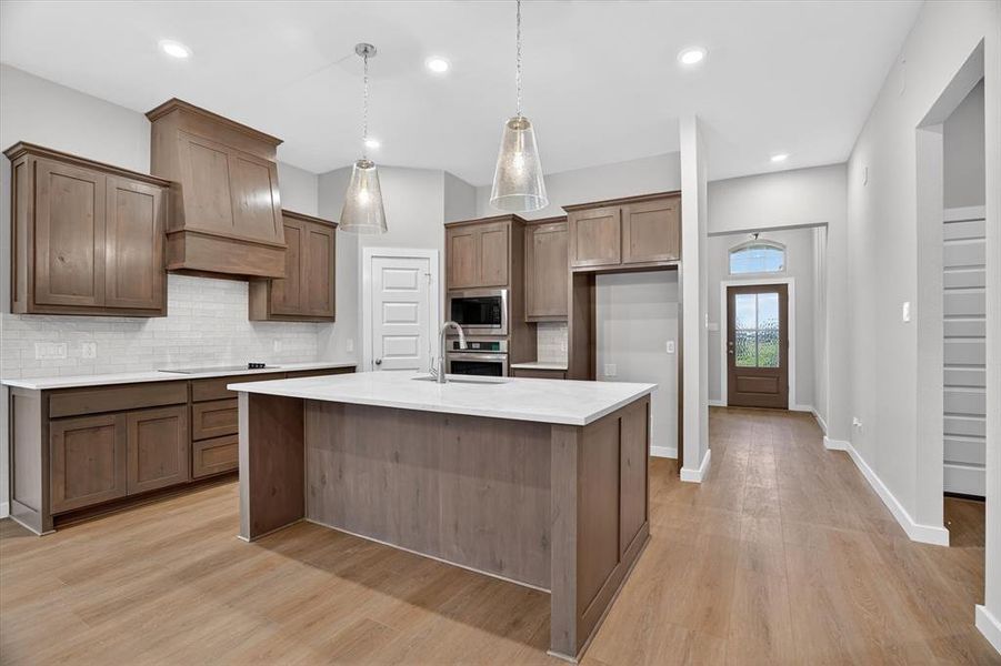 Kitchen featuring a central island with a light-toned countertop, wood-finish flooring, recessed lighting, pendant lighting, and stainless steel built-in appliances