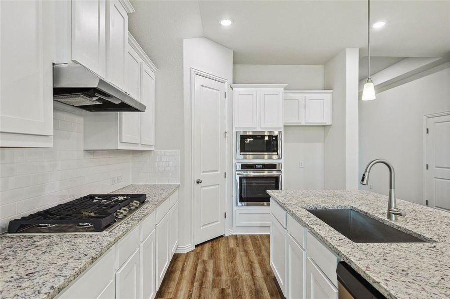 Kitchen featuring wall chimney range hood, appliances with stainless steel finishes, backsplash, wood-type flooring, and sink