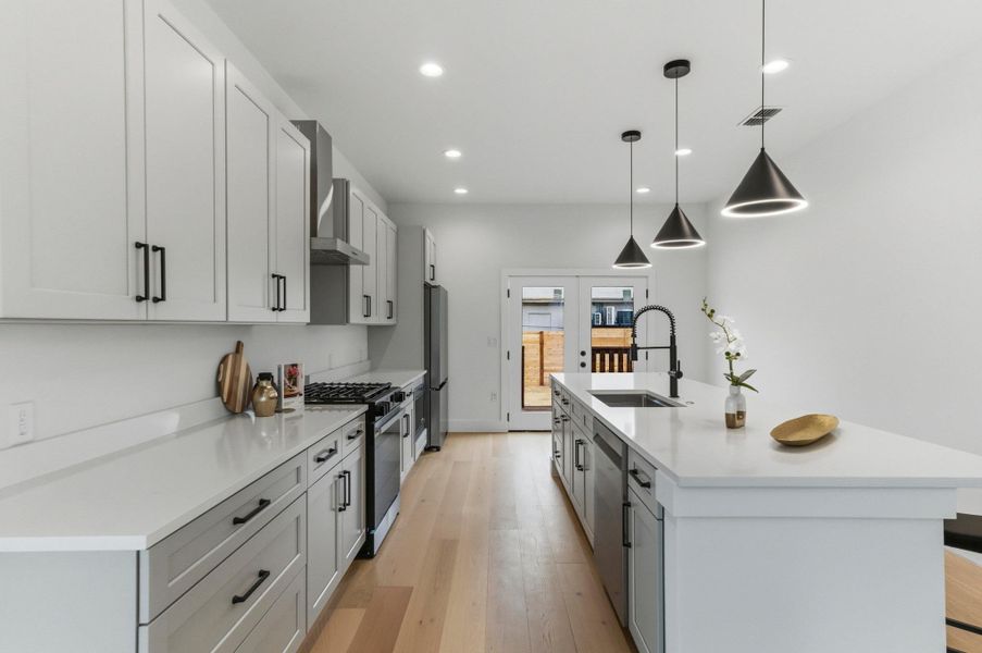 Kitchen featuring a center island with sink, hanging light fixtures, appliances with stainless steel finishes, light wood-style floors, and recessed lighting