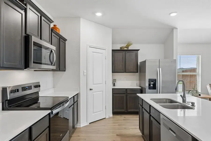 Kitchen with stainless steel appliances, light wood-style flooring, light stone counters, recessed lighting, and dark wood finish cabinets Kitchen with stainless steel appliances, light wood-style flooring, light stone counters, recessed lighting, and dark wood finish cabinets