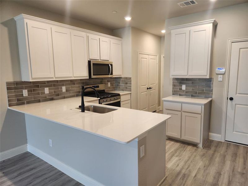 Kitchen with stainless steel appliances, kitchen peninsula, light hardwood / wood-style floors, backsplash, and white cabinetry