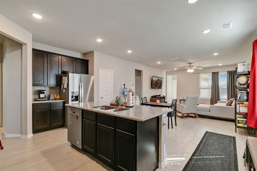 Kitchen with light hardwood / wood-style flooring, stainless steel appliances, a center island with sink, sink, and light stone countertops