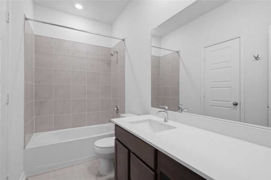 The secondary bathroom showcases tile flooring, a bath/shower combo with Daltile tile surround, a vanity with knee space and a stunning light countertop, large mirror, sleek fixtures, and contemporary finishes throughout. The secondary bathroom showcases tile flooring, a bath/shower combo with Daltile tile surround, a vanity with knee space and a stunning light countertop, large mirror, sleek fixtures, and contemporary finishes throughout.