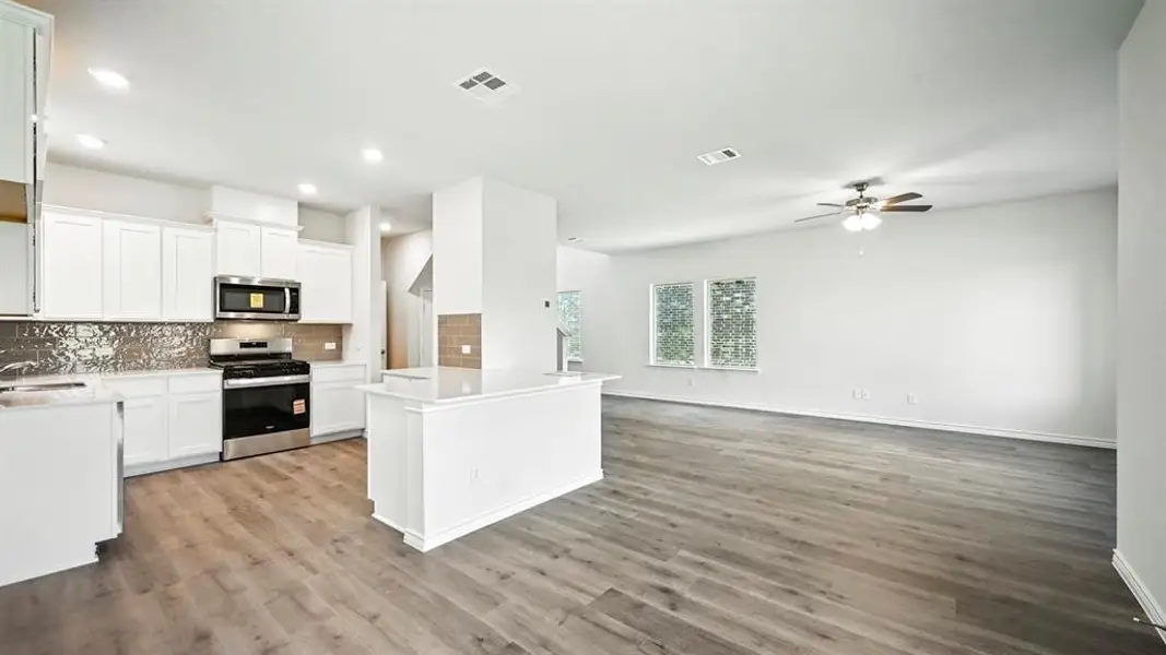 Kitchen with white cabinets, stainless steel appliances, backsplash, open floor plan, and light stone counters