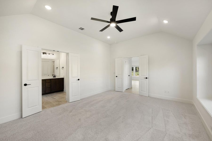 Empty master bedroom with carpet, ceiling fan, and open doors to ensuite bathroom and closet