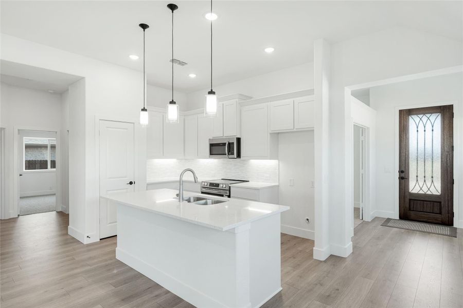 White kitchen with center island, pendant lights, stainless appliances, and light wood floors