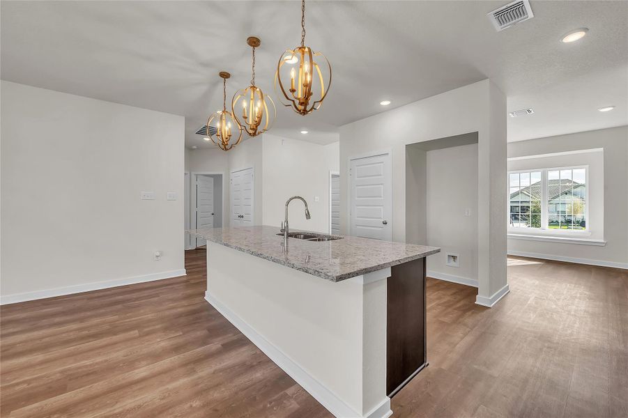 Kitchen with light stone counters, pendant lighting, light wood-style flooring, an island with sink, and recessed lighting Kitchen with light stone counters, pendant lighting, light wood-style flooring, an island with sink, and recessed lighting