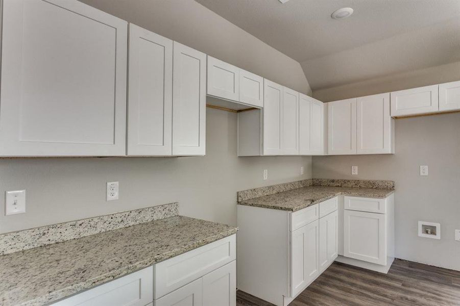 Kitchen with white cabinetry, vaulted ceiling, dark wood-style floors, and light stone countertops