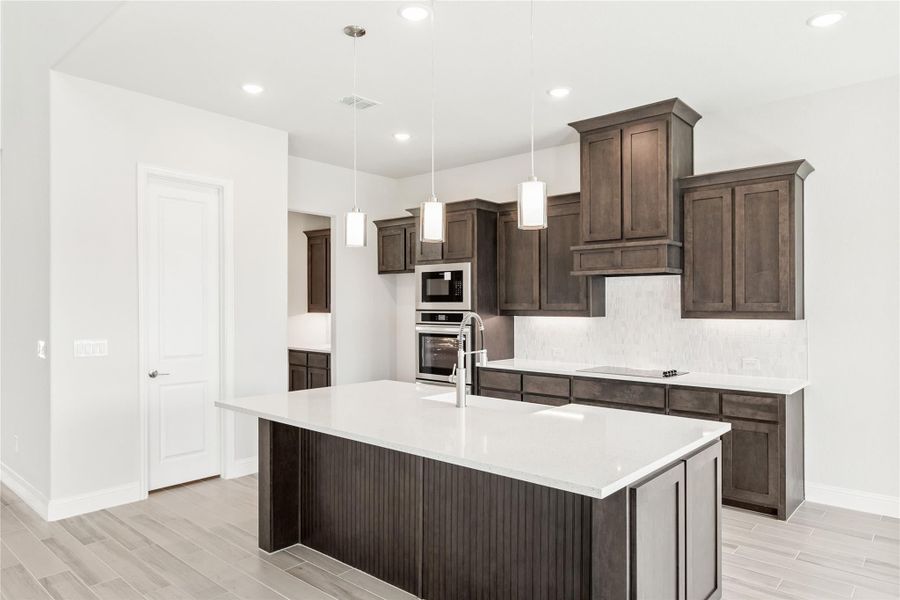 Kitchen with dark wood cabinets, large center island, white countertops, and stainless steel appliances Kitchen with dark wood cabinets, large center island, white countertops, and stainless steel appliances