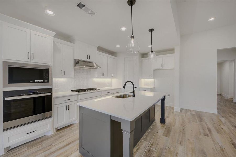 Modern kitchen featuring white cabinetry, stainless steel appliances, a center island with pendant lighting, and wood-finish flooring