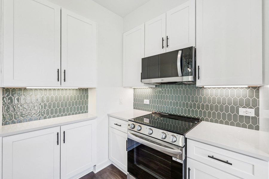 Kitchen featuring stainless steel appliances, white cabinetry, tasteful backsplash, and light stone countertops Kitchen featuring stainless steel appliances, white cabinetry, tasteful backsplash, and light stone countertops