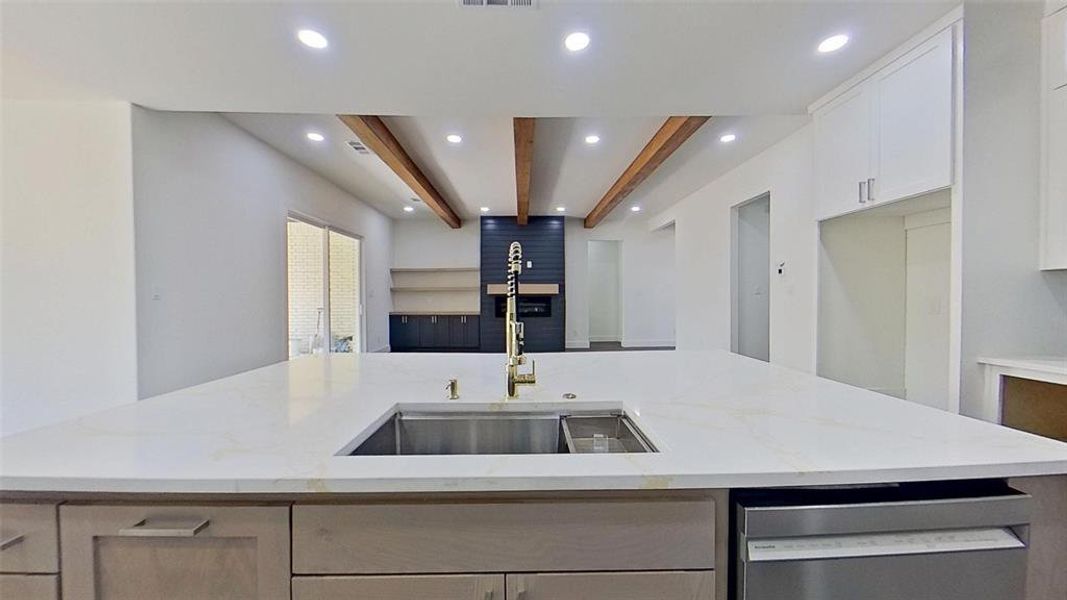 Kitchen featuring light stone counters, beam ceiling, stainless steel dishwasher, a center island with sink, and recessed lighting