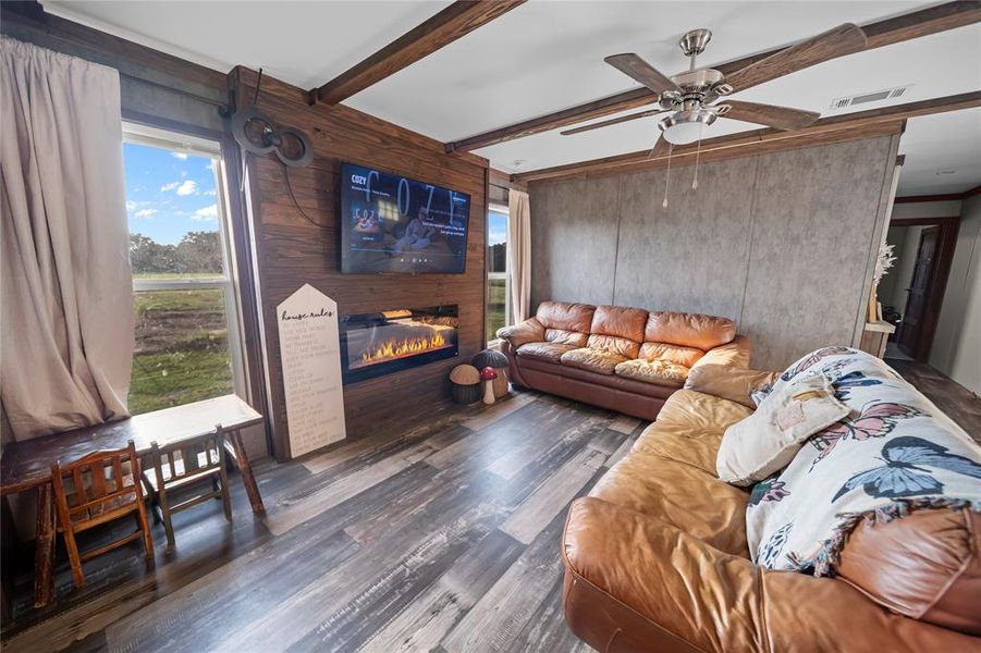Living area with wood walls, beam ceiling, a glass covered fireplace, wood finished floors, and plenty of natural light Living area with wood walls, beam ceiling, a glass covered fireplace, wood finished floors, and plenty of natural light