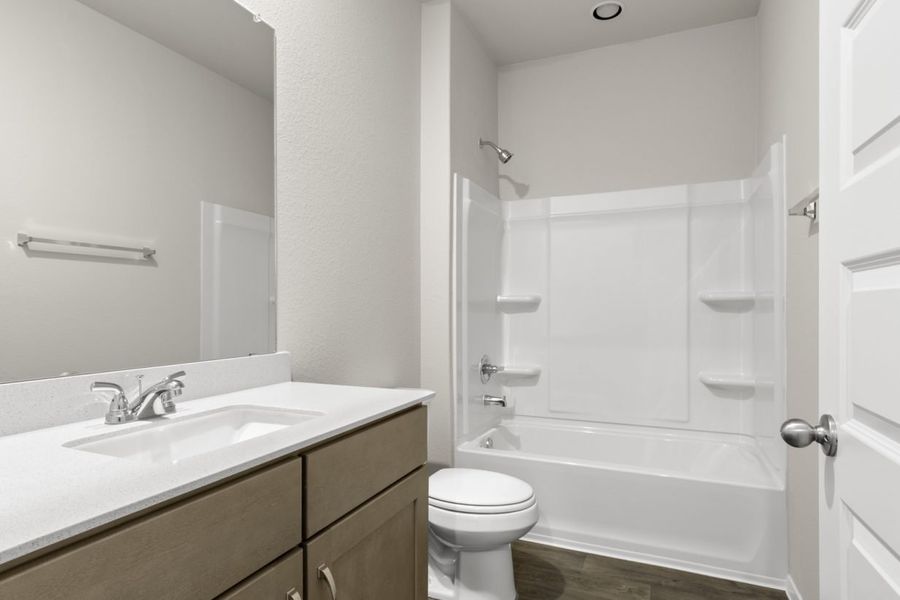 Image of a bathroom with light brown cabinets, a white vanity, a large mirror and a white shower and tub