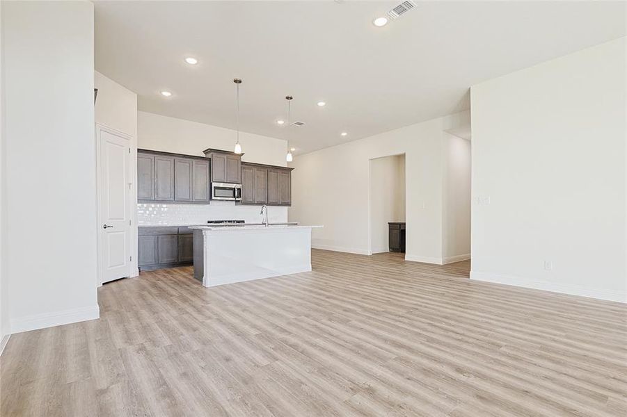 Kitchen with sink, hanging light fixtures, backsplash, light hardwood / wood-style floors, and a kitchen island with sink