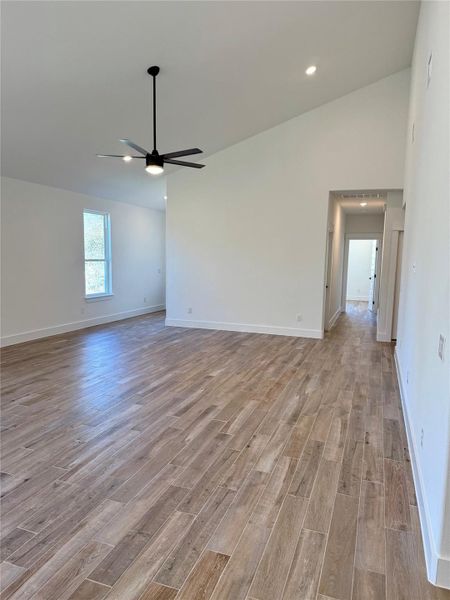 Spare room with lofted ceiling, light wood-style floors, and a ceiling fan