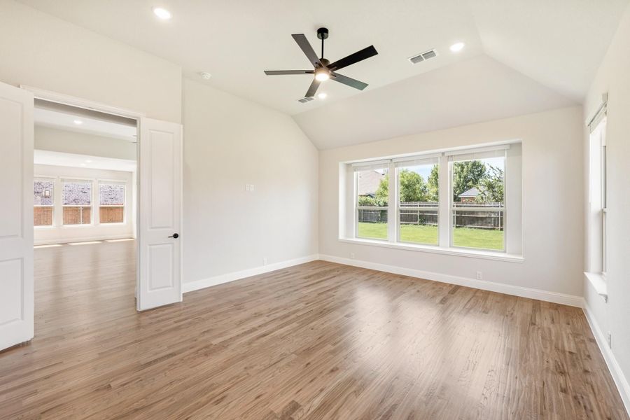 Empty bedroom with vaulted ceiling, ceiling fan, hardwood floors, and large backyard-facing window Empty bedroom with vaulted ceiling, ceiling fan, hardwood floors, and large backyard-facing window