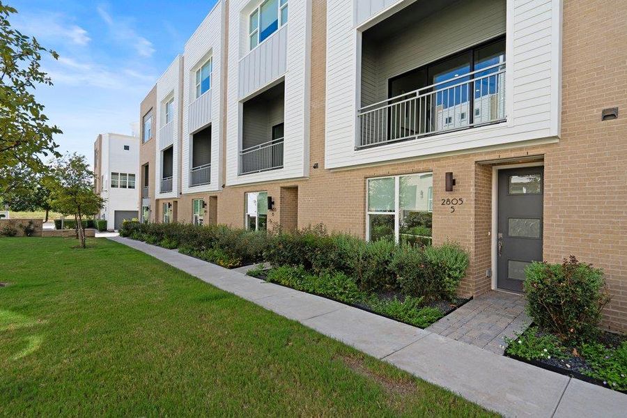 A concrete walkway leads to the entrance of a modern multi-level brick and siding townhouse. A concrete walkway leads to the entrance of a modern multi-level brick and siding townhouse.