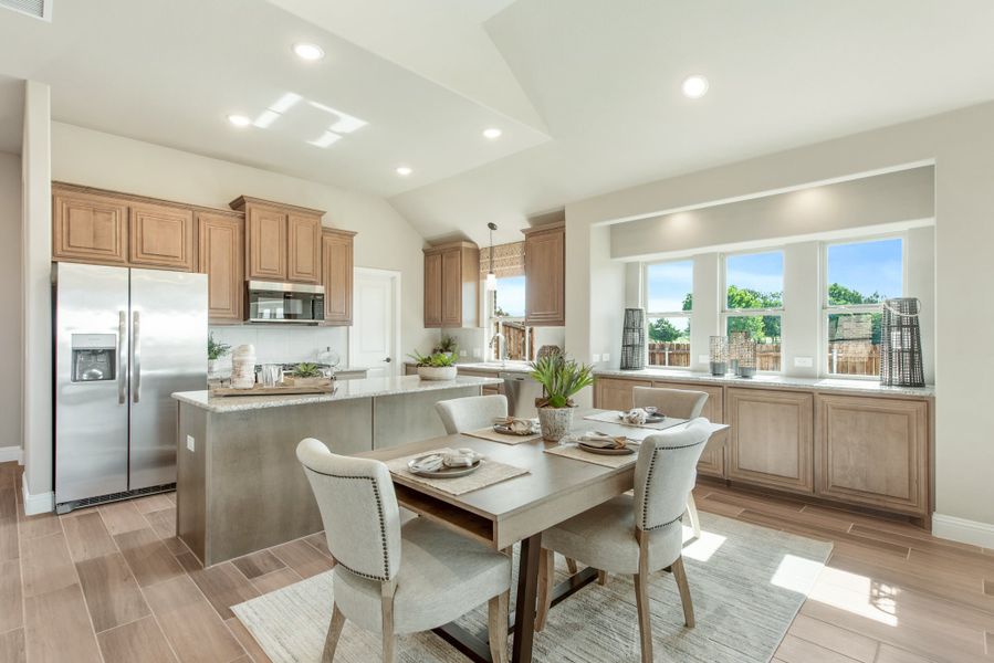 Open kitchen and dining area with wood cabinets, kitchen island, stainless appliances, and dining table for four near large windows