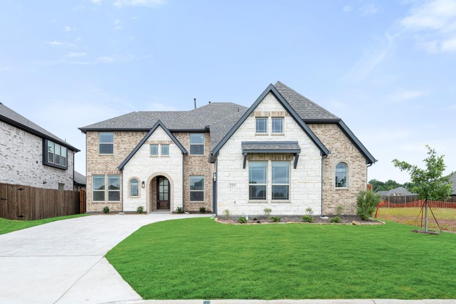 Two-story home with brick and stone exterior, arched entry, and curved driveway with green lawn