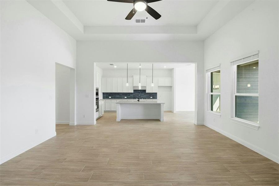 Open-concept living area featuring wood-finish tile flooring, a tray ceiling, and a ceiling fan