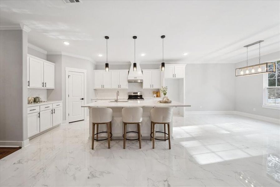 Kitchen with white cabinetry, custom exhaust hood, stainless steel electric range oven, a center island with sink, and pendant lighting