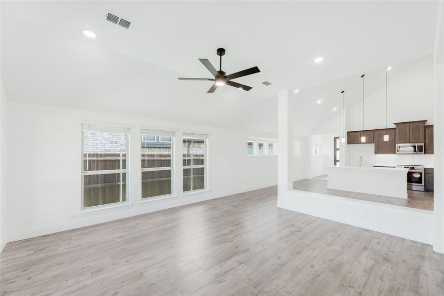 Open living room with light wood floors and ceiling fan, open to kitchen with dark cabinets and stainless appliances Open living room with light wood floors and ceiling fan, open to kitchen with dark cabinets and stainless appliances