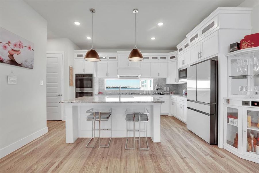 Kitchen with stainless steel appliances, a kitchen island, pendant lighting, light hardwood / wood-style floors, and white cabinets